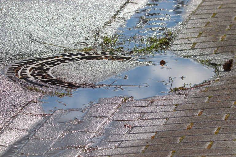 Manhole cover in a roadway with pooled rainwater illustrating wet-weather inflow risk and manhole I&I.