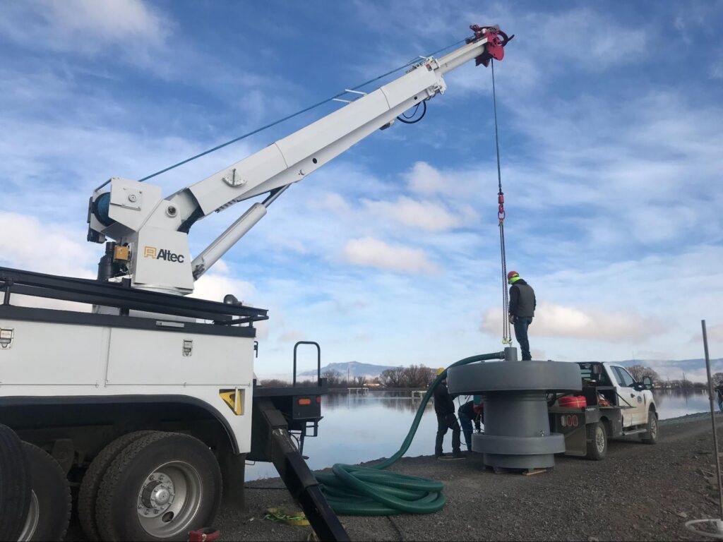 Crew servicing a lagoon aerator on the bank with a small truck-mounted crane.