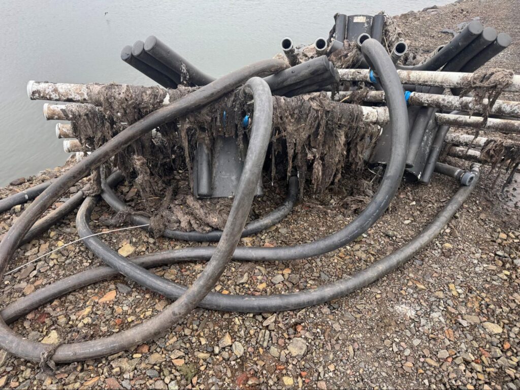 Fouled lagoon diffuser assemblies pulled to the bank, hung with rags and sludge.