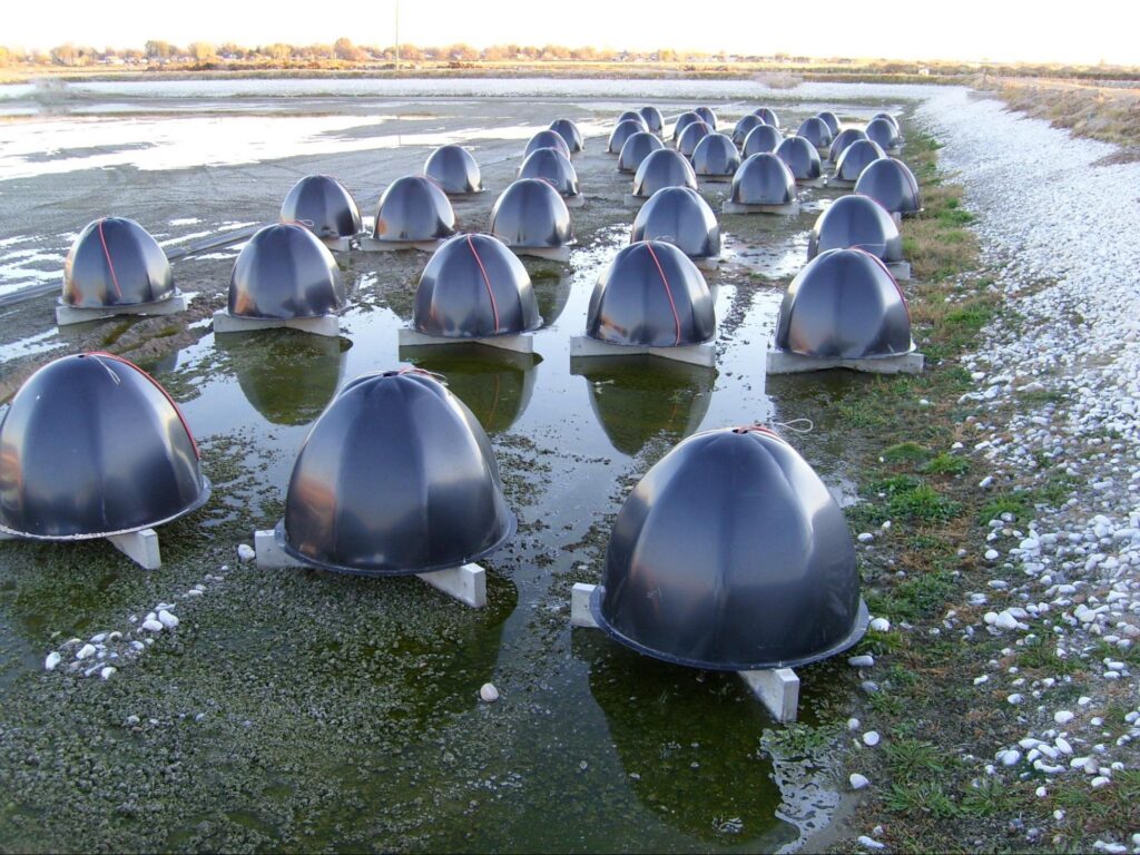 Dozens of dome diffusers on concrete anchors sitting exposed in a drained wastewater lagoon.