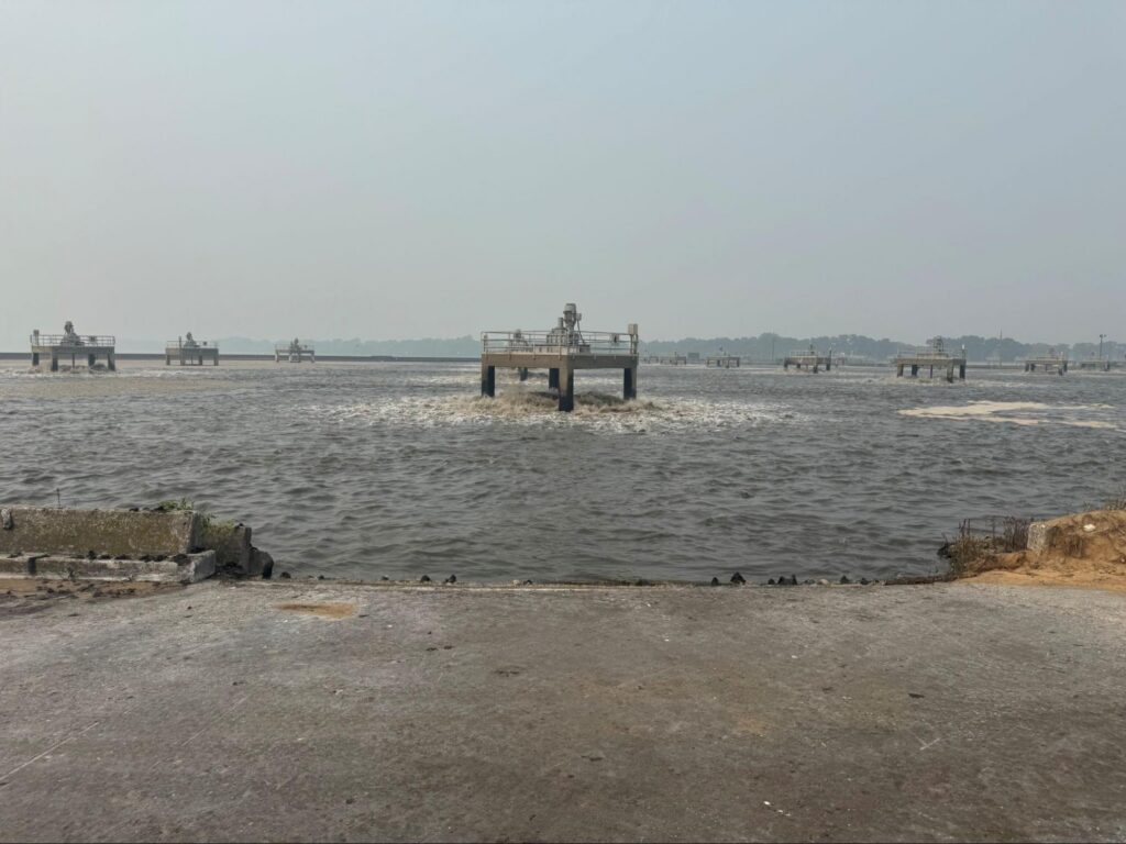 Platform-mounted low-speed surface aerators offshore in a wastewater lagoon, viewed from the bank.