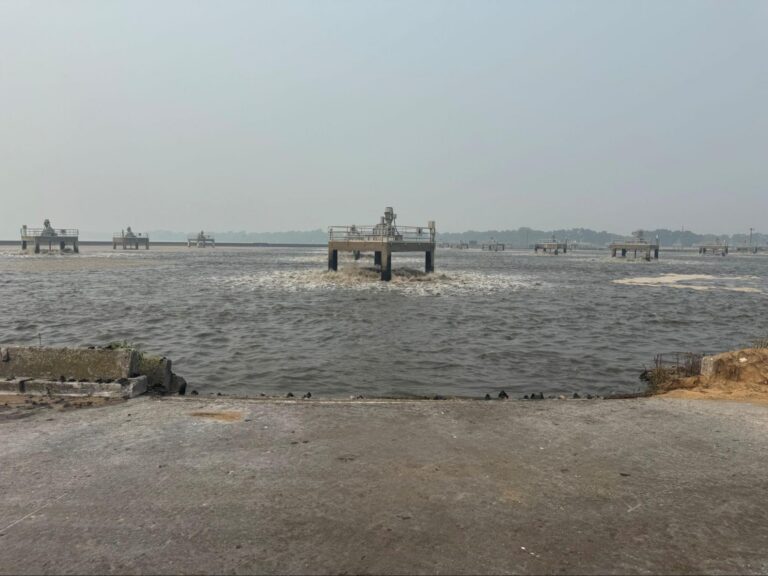 Platform-mounted low-speed surface aerators offshore in a wastewater lagoon, viewed from the bank.
